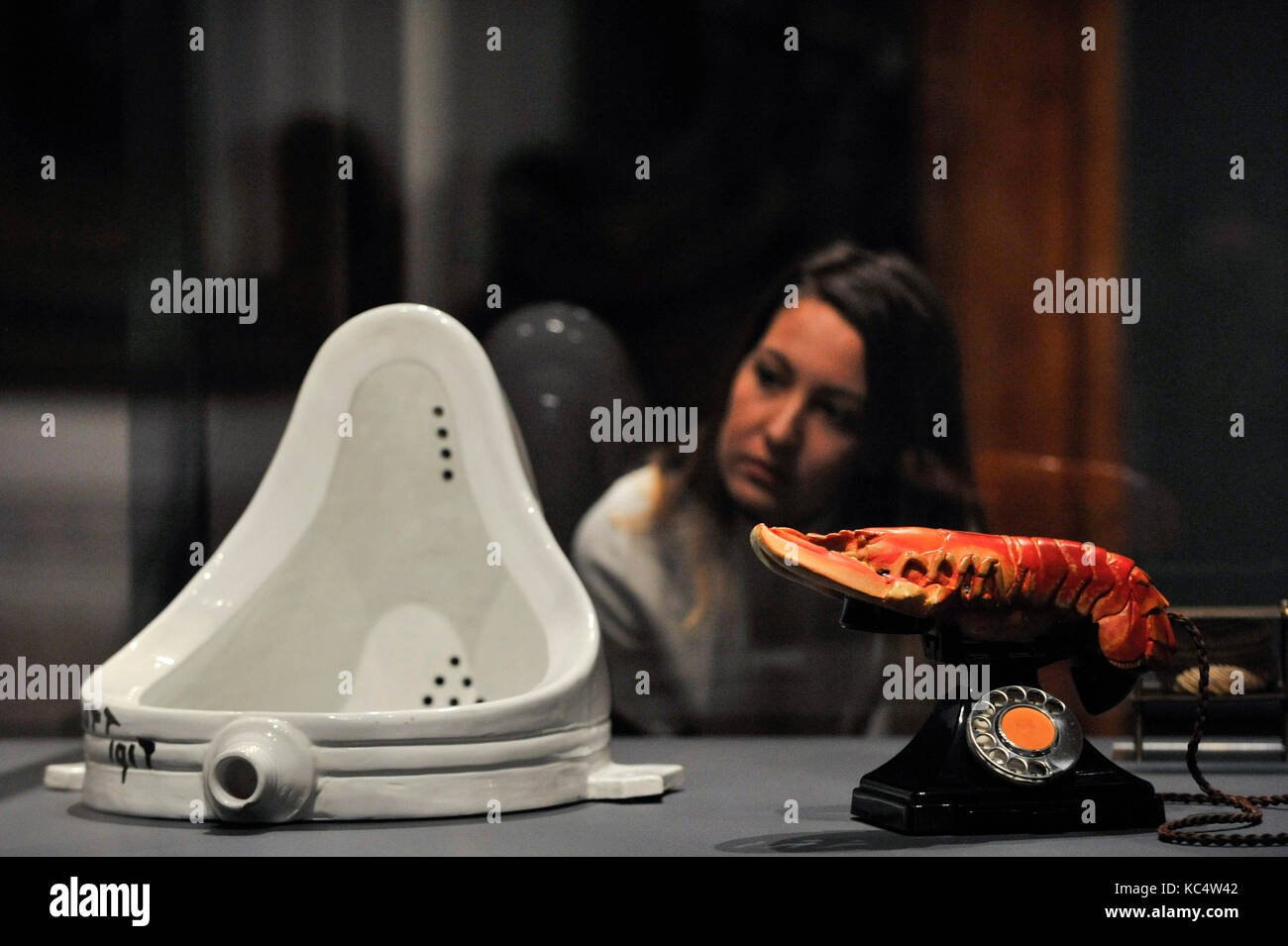 London, UK.  3 October 2017.  A staff member views (L to R) 'Fountain, 1917', 1964 edition, by Michel Duchamp and 'Lobster Telephone (red)', 1938, by Salvador Dali with Edward James at the preview of 'Dali / Duchamp', a new exhibition of works by Salvador Dali and Michel Duchamp taking place at the Royal Academy of Arts in Piccadilly.  Over 80 artworks in different media are on display from 7 October to 3 January 2018. Credit: Stephen Chung / Alamy Live News Stock Photo