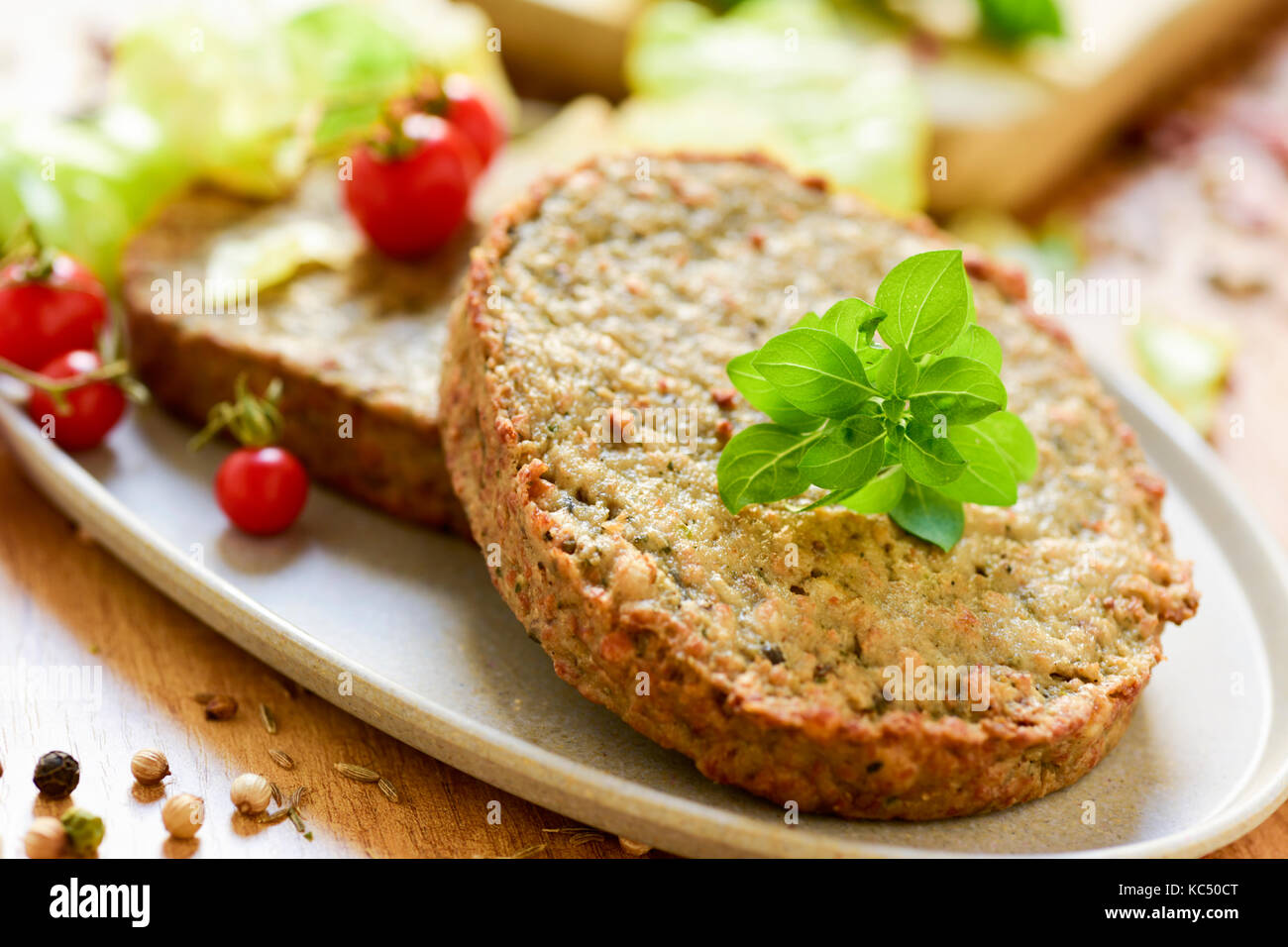 closeup of some veggie burgers made with eggplants and other vegetables in a plate, placed on a rustic wooden table Stock Photo