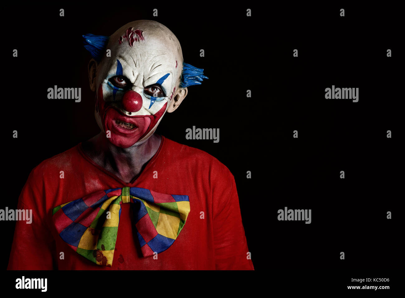 closeup of a scary evil clown wearing a dirty and ragged costume with a blank black space on the right Stock Photo