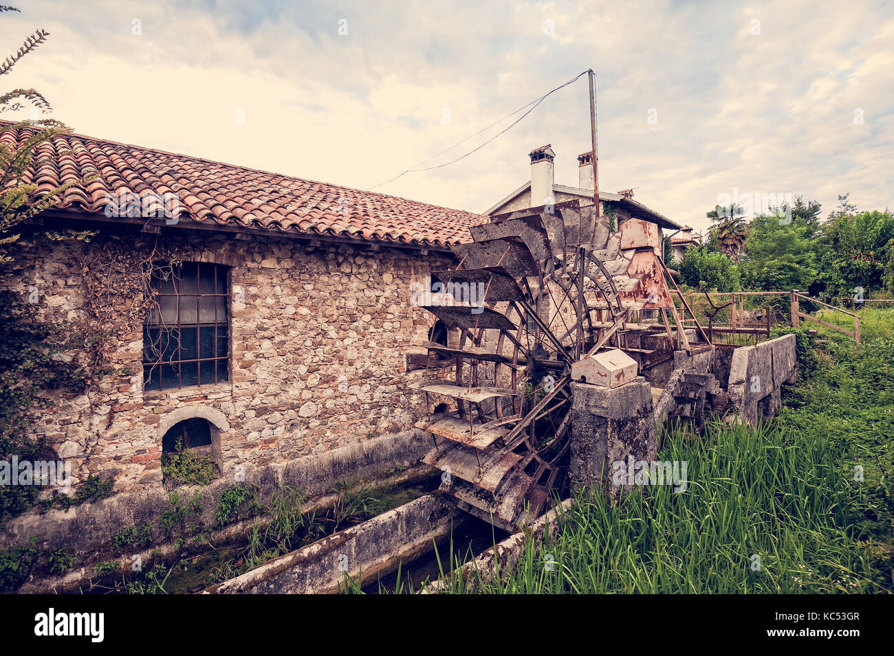 Old water mill with iron water wheel. Photo in vintage style. Stock Photo
