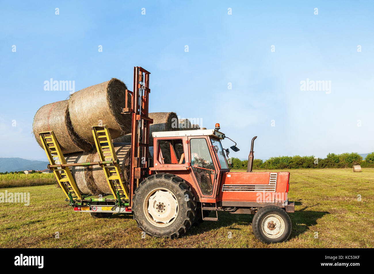 Tractor lifting hay bale on barrow.Agricultural landscape Stock Photo