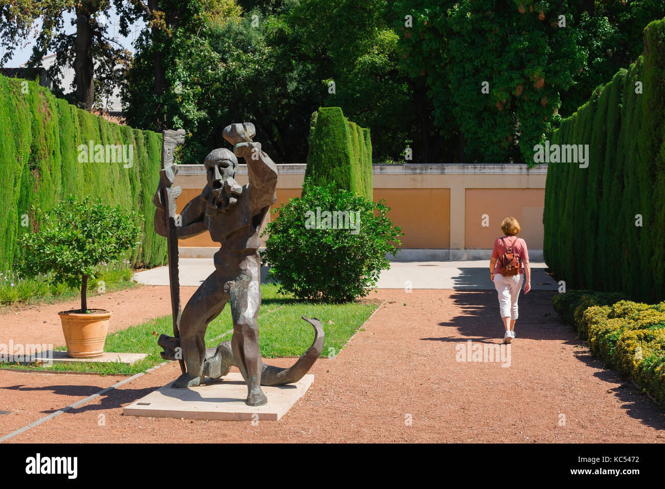 Formal garden, rear view of a solo woman traveler walking past a modernist statue of Hercules in the Jardin de las Hesperides, Valencia, Spain Stock Photo