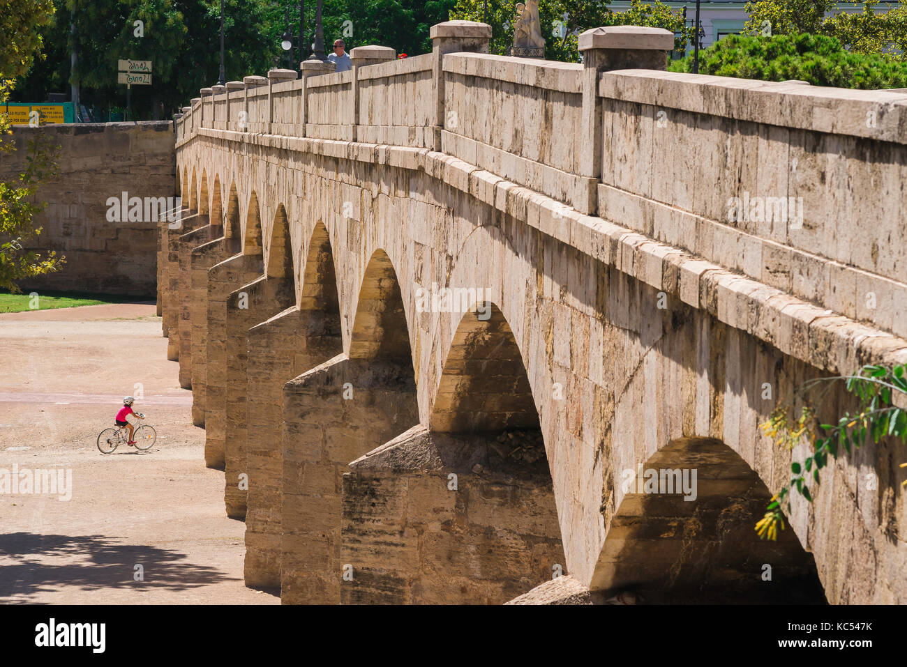 Valencia Turia Garden, view of a young cyclist approaching the arches of the Trinidad bridge in the Jardines del Turia riverbed park, Valencia, Spain. Stock Photo