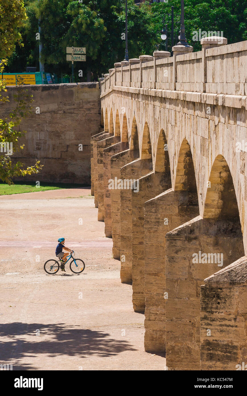 Valencia Turia Garden, a young cyclist approaches the arches of the Trinidad bridge in the Jardines del Turia riverbed park, Valencia, Spain. Stock Photo