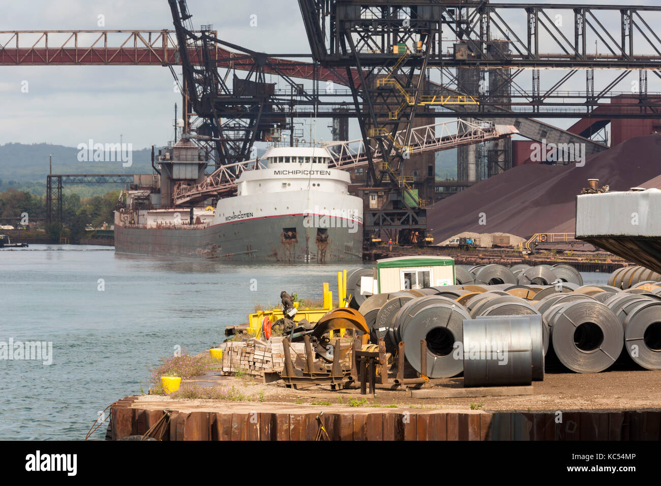 Sault Ste. Marie, Ontario Canada - Steel rolls on the dock at the Algoma steel mill on the shore of the St. Mary's River. Down the dock, the bulk carg Stock Photo