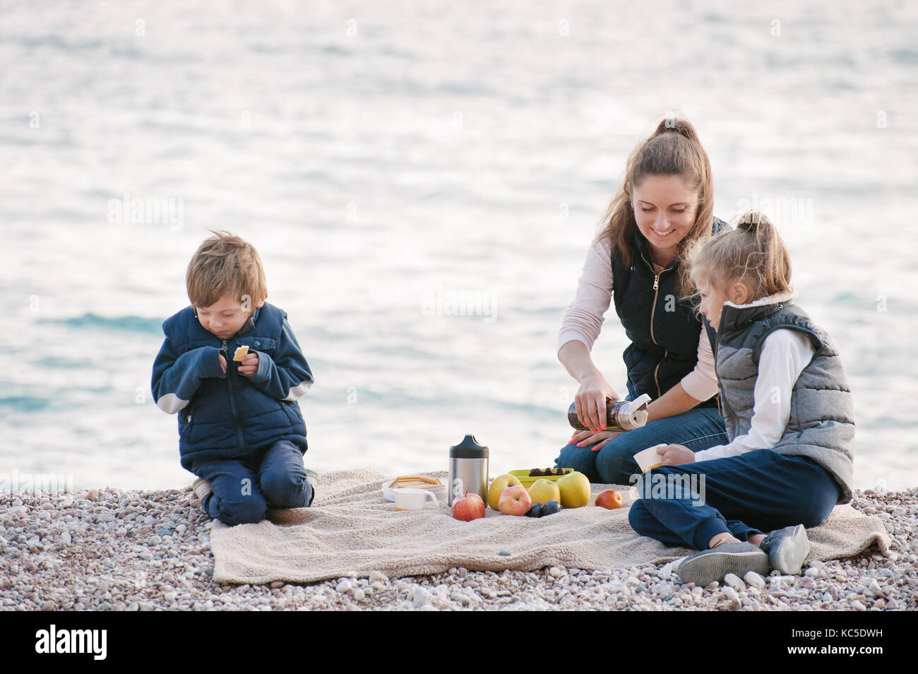 happy mother with two kids on a picnic by the sea in autumn Stock Photo
