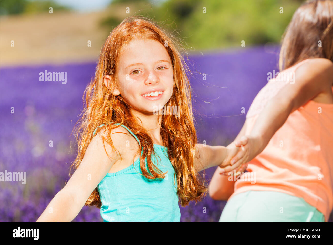 Portrait of preteen red-headed girl holding hand of her friend while walking in lavender field Stock Photo