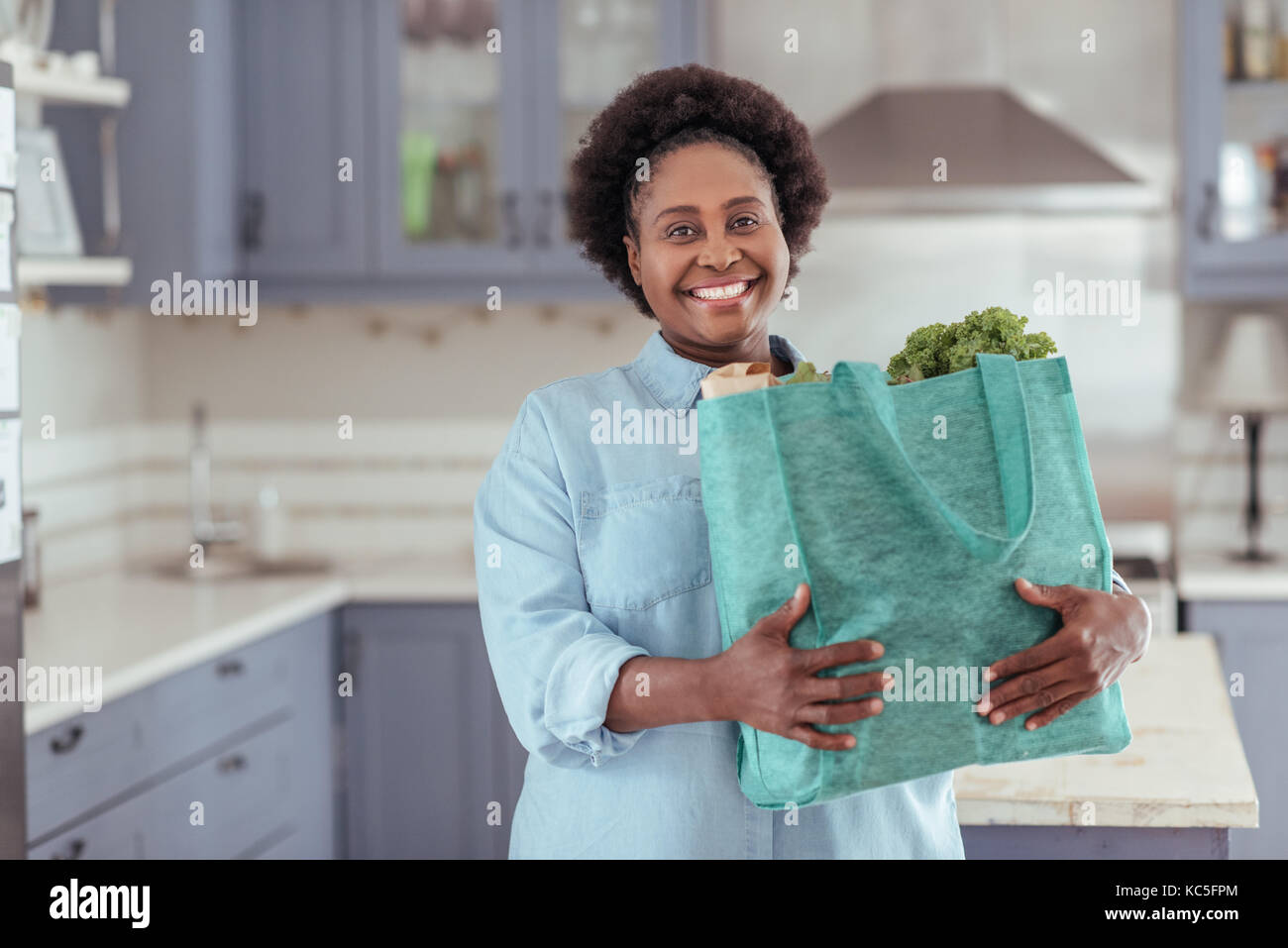 Smiling young African woman standing in her kitchen with groceries Stock Photo