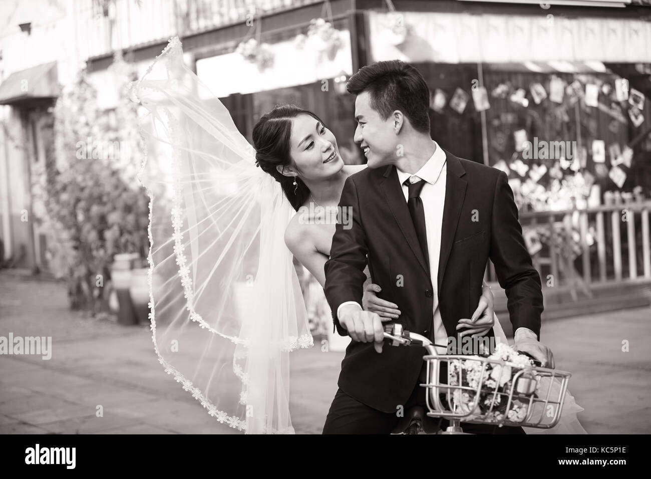 romantic asian newly wed couple having fun riding a bicycle together, black and white. Stock Photo