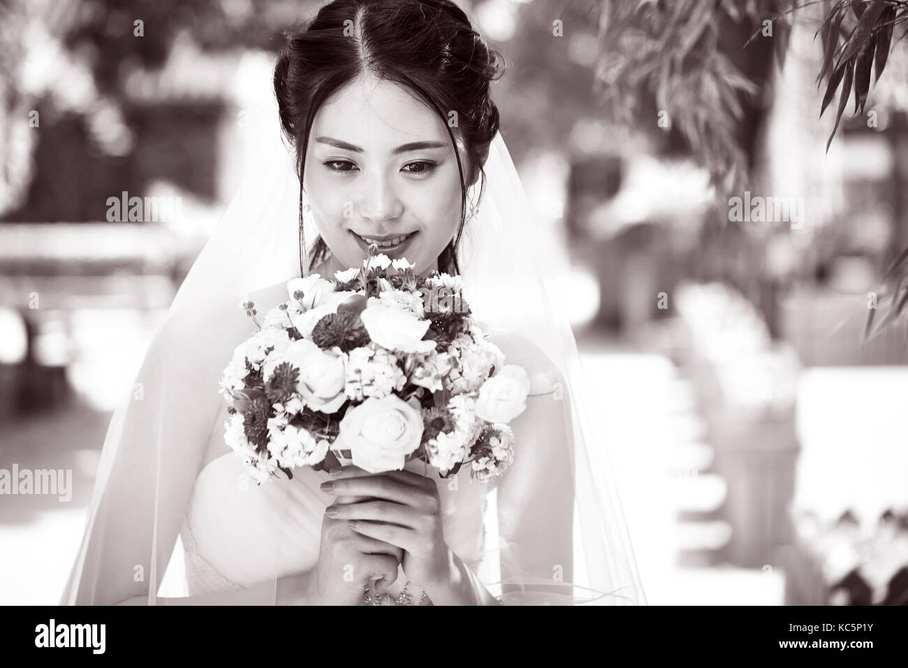 beautiful and happy young asian bride wearing wedding dress holding a bunch of flower, black and white. Stock Photo