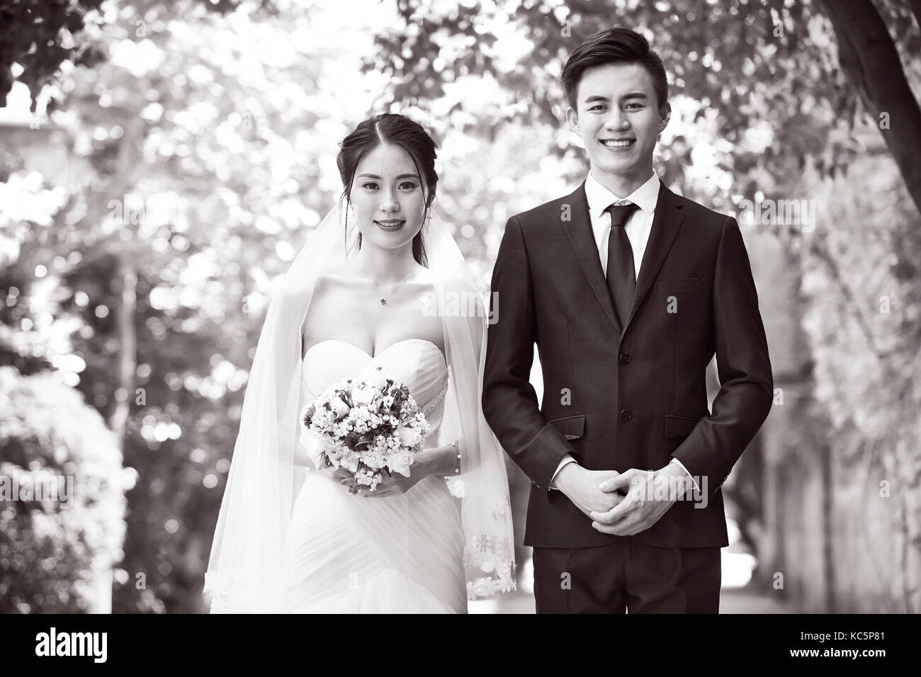 outdoor portrait of asian bride and groom looking at camera smiling, black and white. Stock Photo