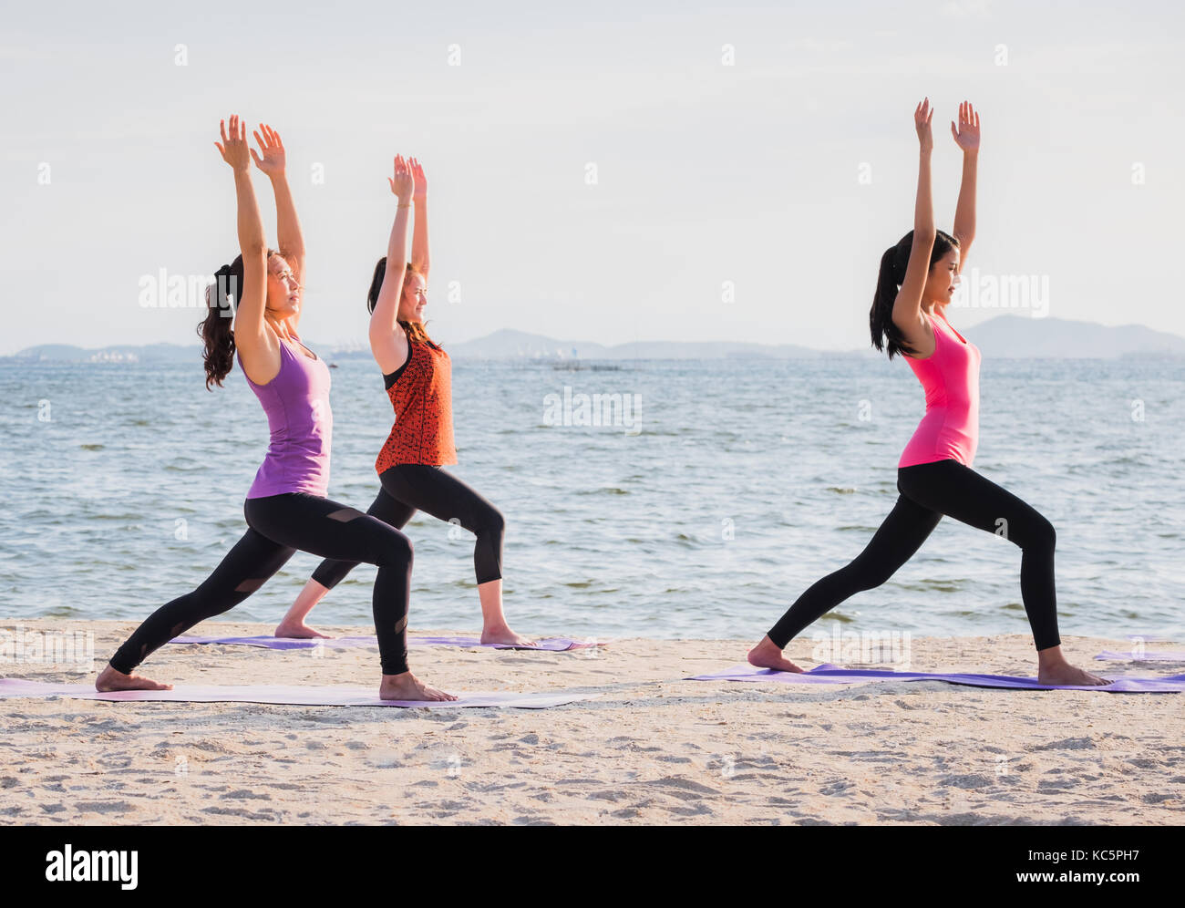 Yoga class at sea beach in evening ,Group of people doing Warrior poses with clam relax emotion at beach,Meditation pose,Wellness and Healthy balance  Stock Photo