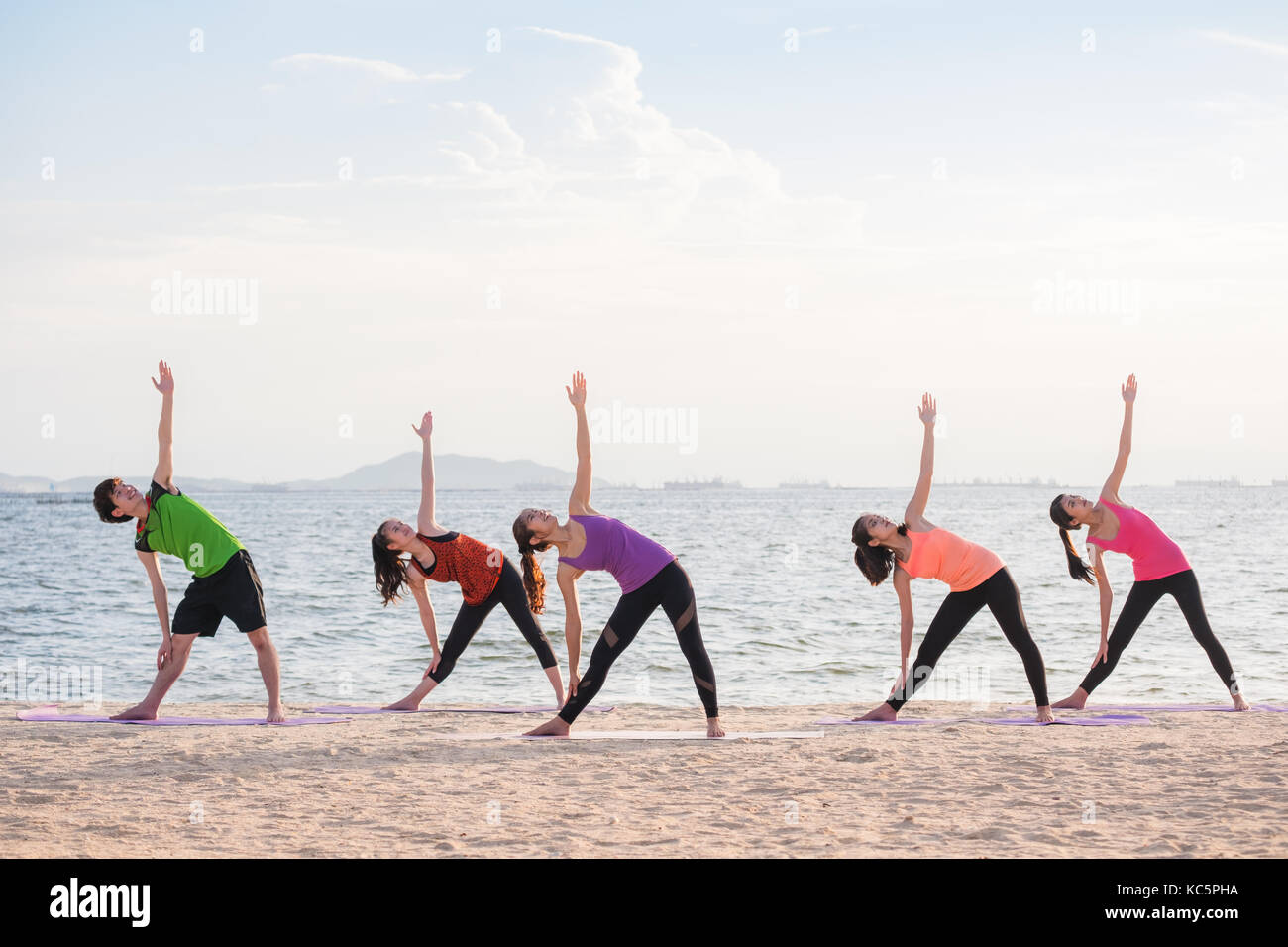 Yoga class at sea beach in evening ,Group of people doing Triangle poses with clam relax emotion at beach,Meditation pose,Wellness and Healthy balance Stock Photo