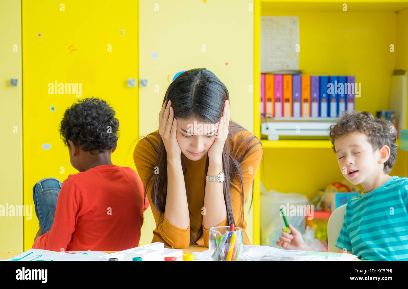 Teacher get headache with two naughty kids in classroom at kindergarten school Stock Photo
