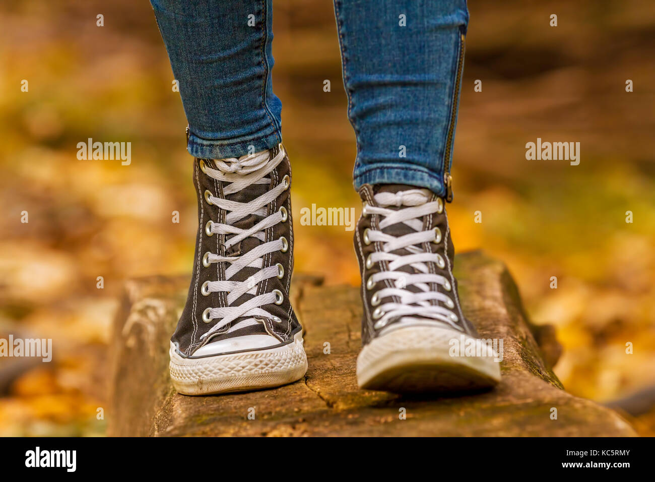 Teenage girl wears with black sneakers walking on wood over fall leaves in the autumn season. Stock Photo