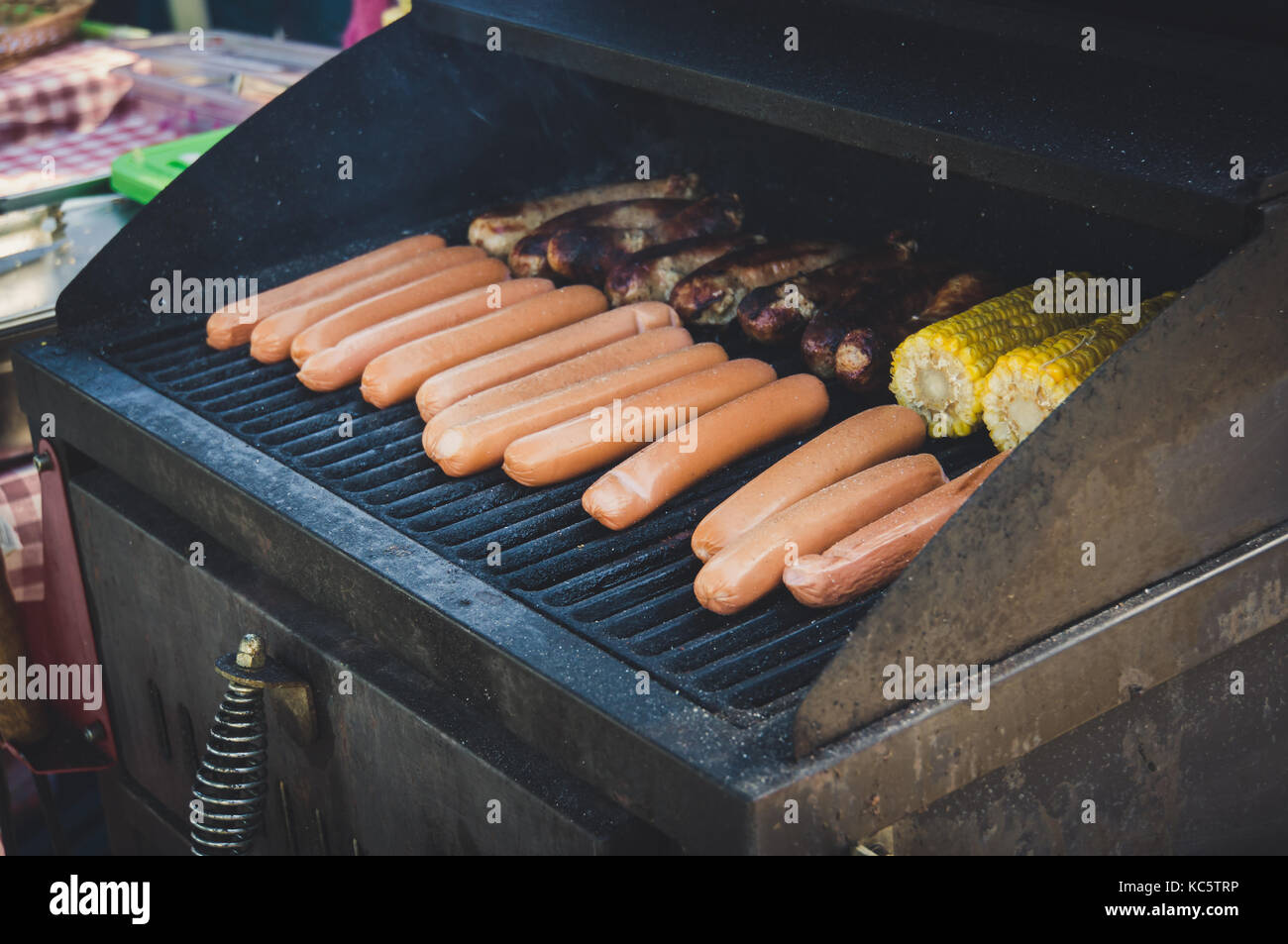 Fresh sausage. Hot dogs grilling outdoors on a gas barbecue grill with vegetables eggplant with corn and potatoes Stock Photo