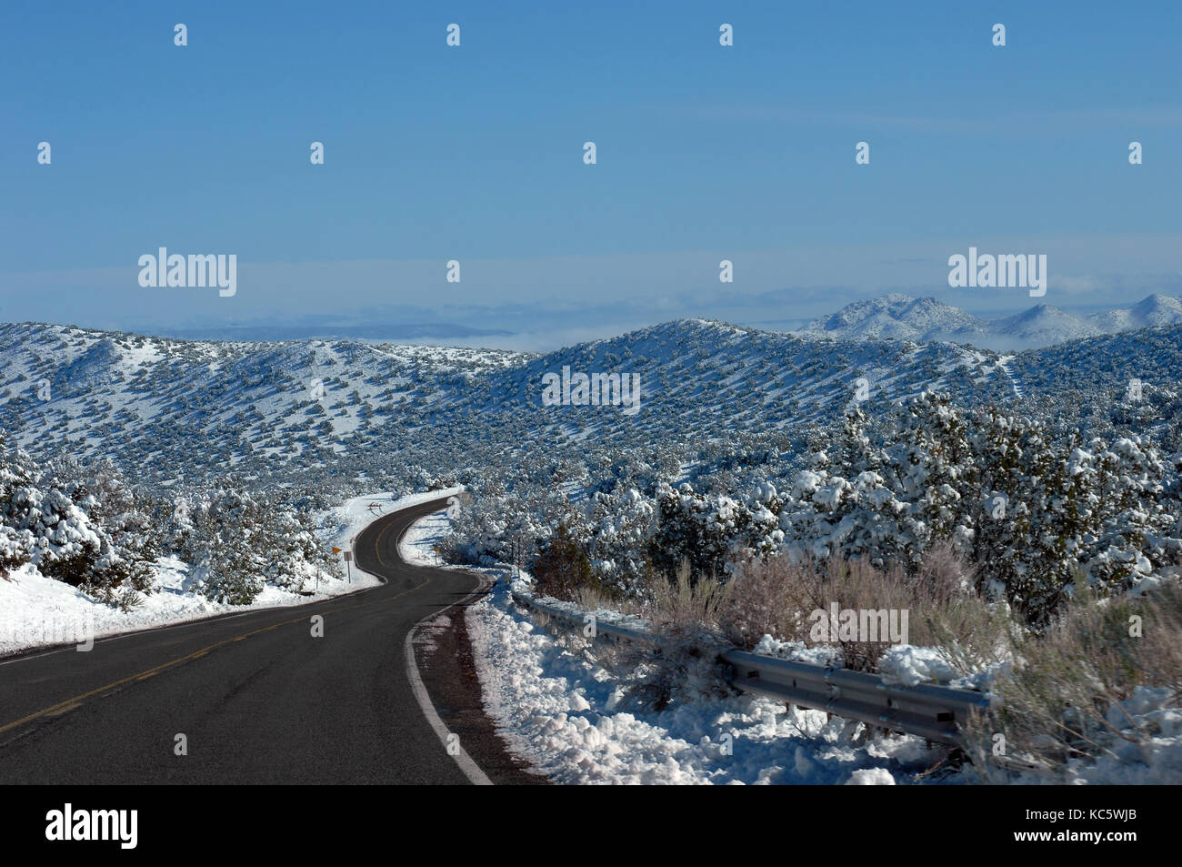 S shaped curving road disappears into the mountaijns of central New Mexico.  Snow covers mountains and trees.  Blue sky. Stock Photo