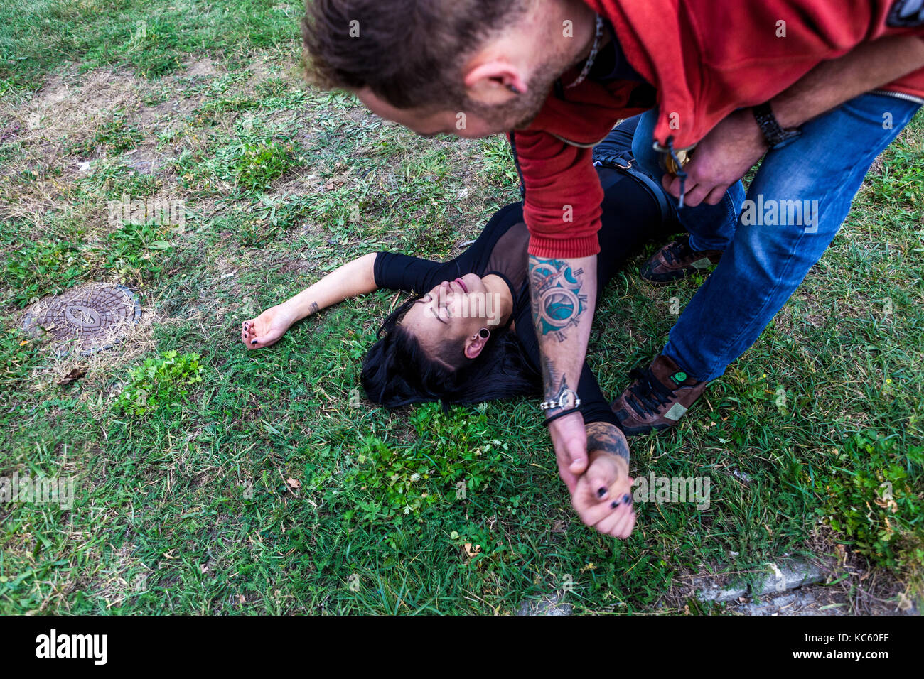The man helping up the young drunk woman lying on the ground drank too much Stock Photo