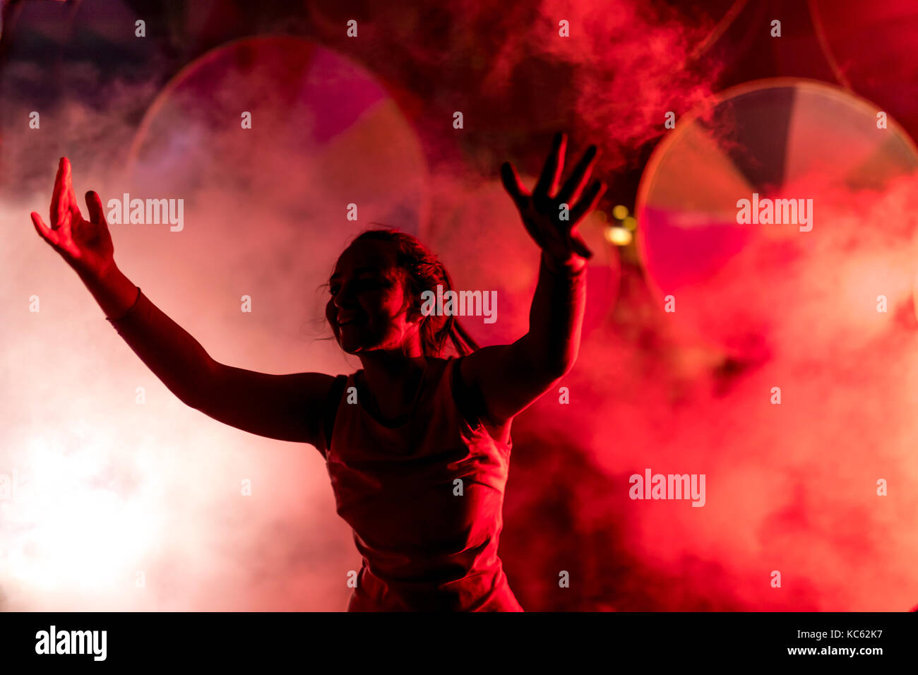 Silhoutte of a festival goer with arms in the air against a smoke ...