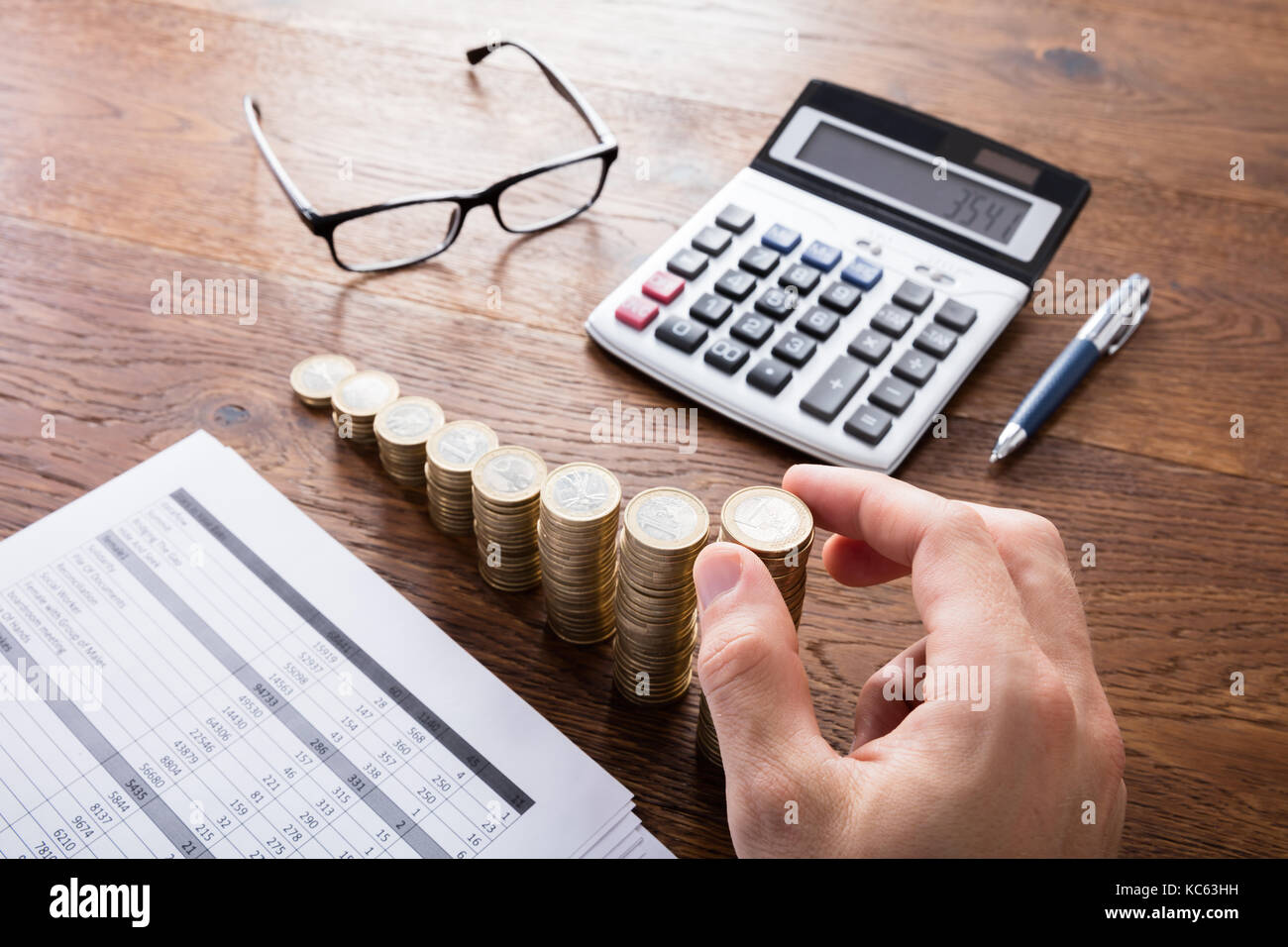 Person Stacking Coins With Calculator And Eyeglasses On Wooden Desk. Income Tax Rise Concept Stock Photo