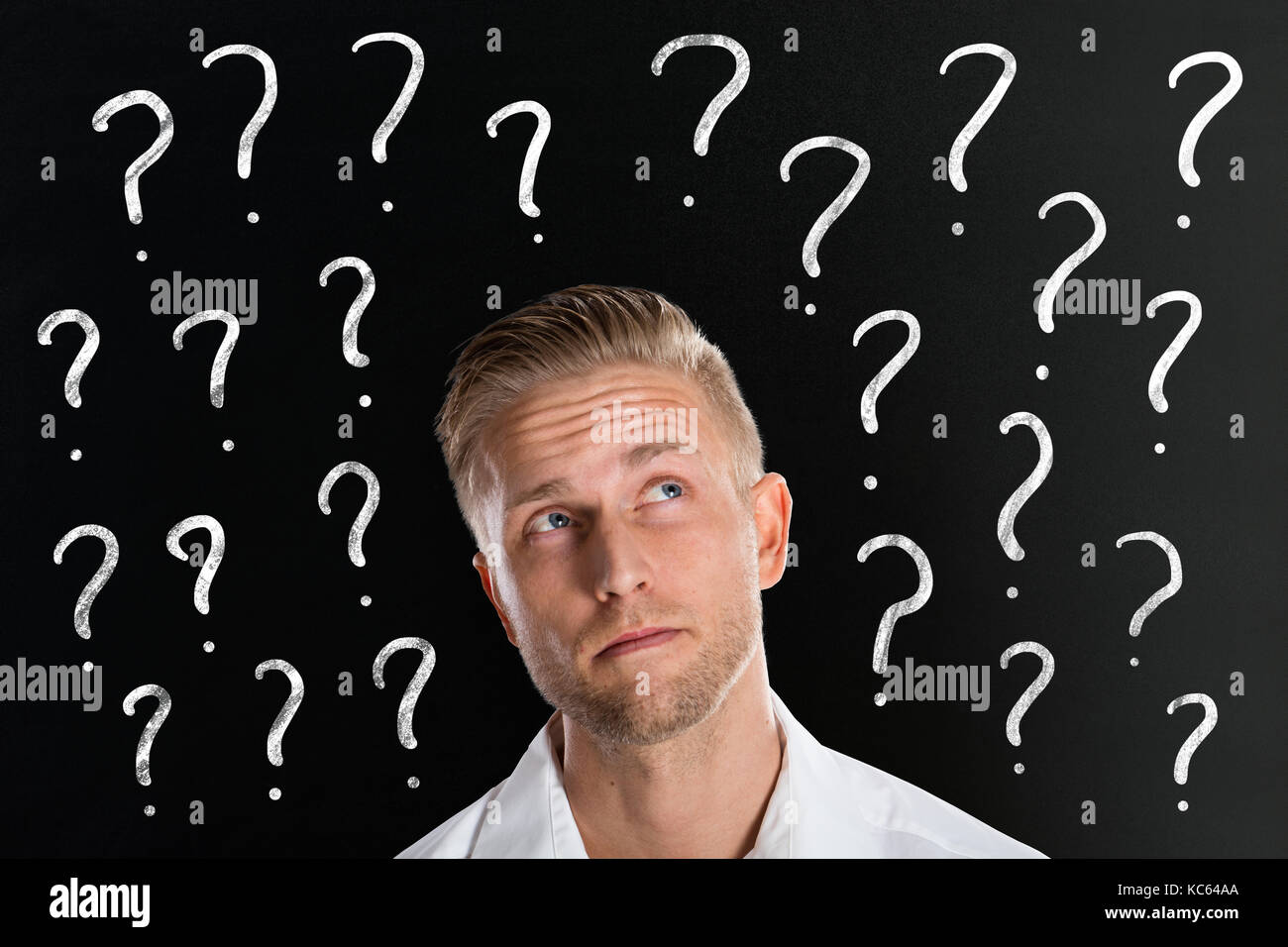 Thinking Young Man In Front Of Question Marks Drawn On Blackboard Stock Photo