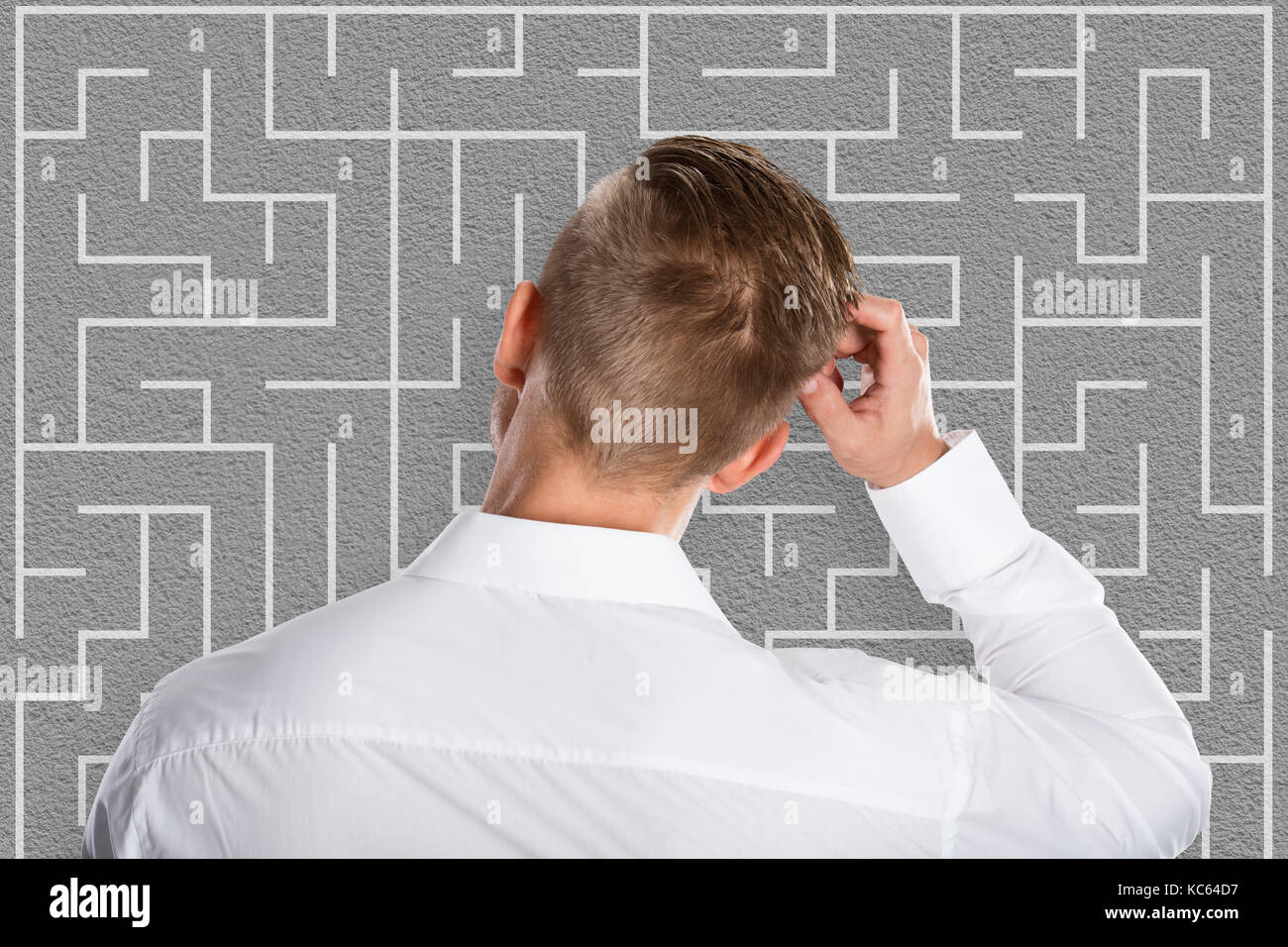 Confused Young Businessman Looking At Labyrinth Trying To Solve Business Puzzle Stock Photo