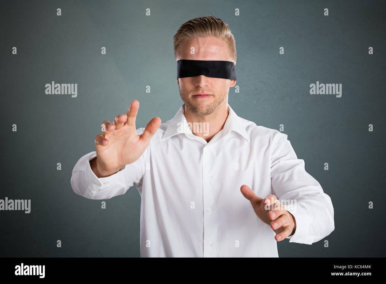 Young Blindfolded Lost Businessman Against Grey Background Stock Photo