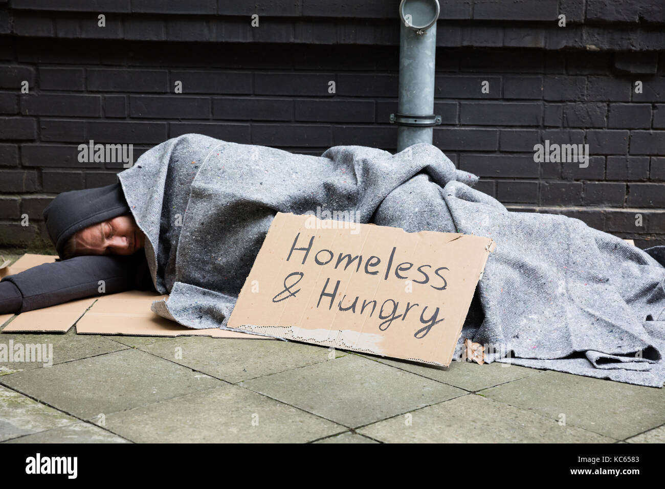 Homeless And Hungry Man Sleeping On Street With Begging Signboard Stock Photo
