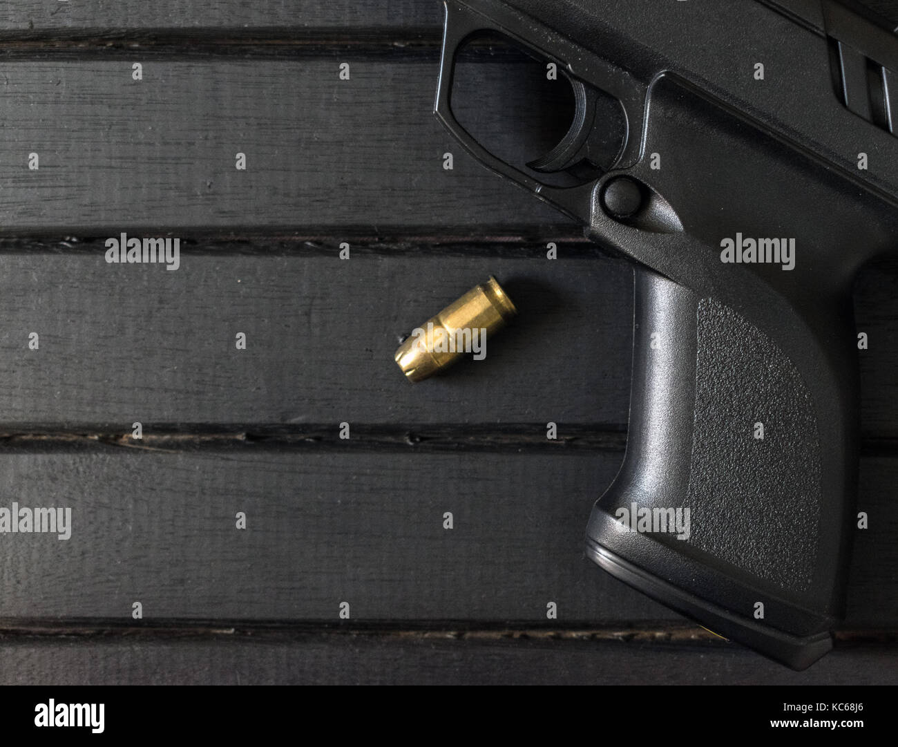 Polymer pistol and .45 caliber round on a black wooden surface, closeup, showing trigger and textured grip Stock Photo