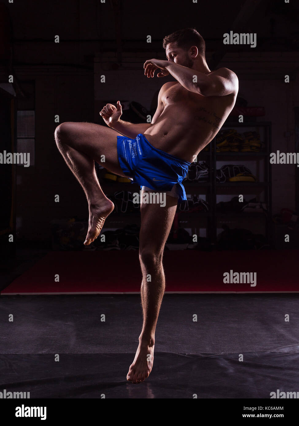 A male MMA fighter training kicks and punches in a dark gym Stock Photo