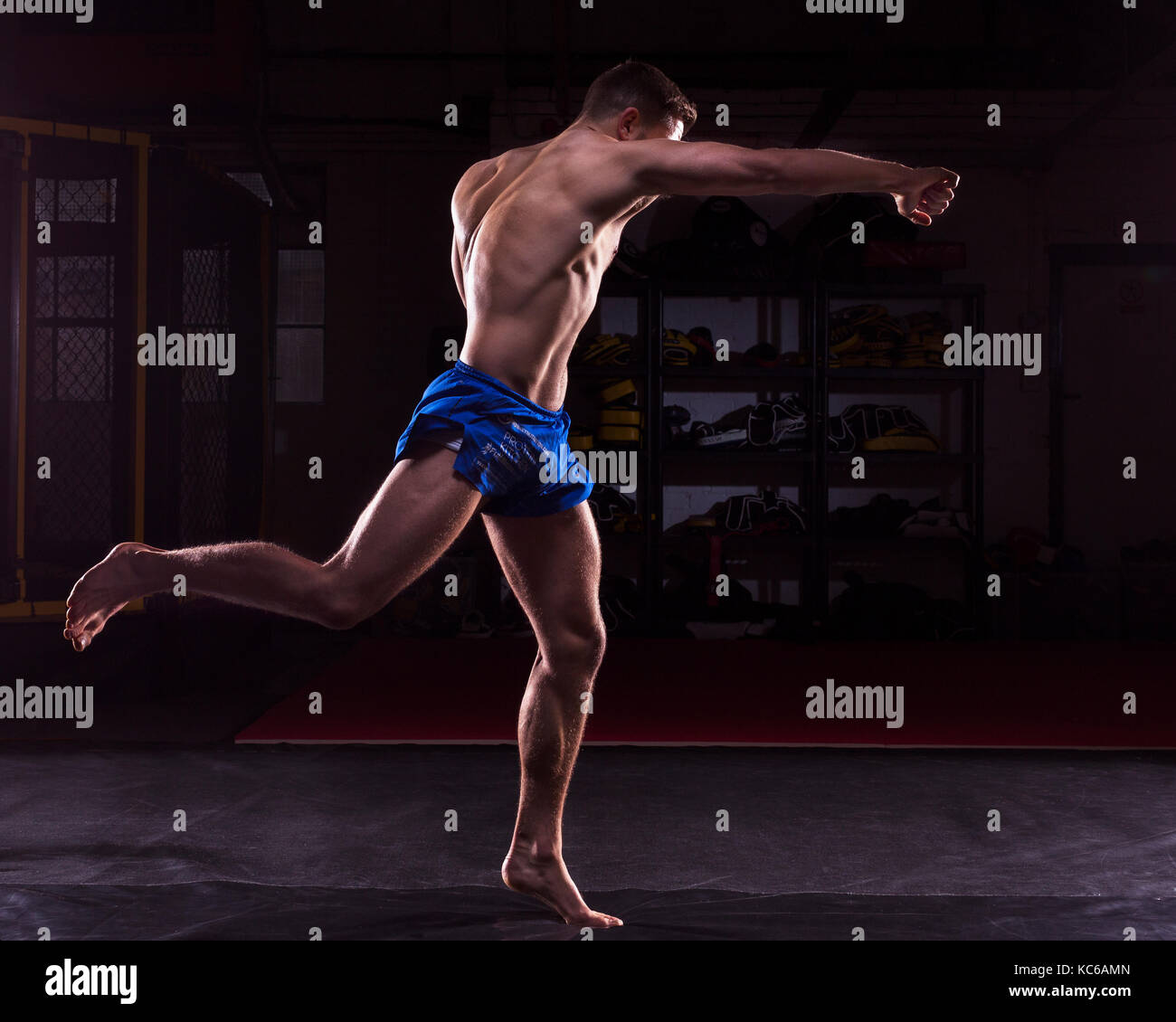 A male MMA fighter training kicks and punches in a dark gym Stock Photo