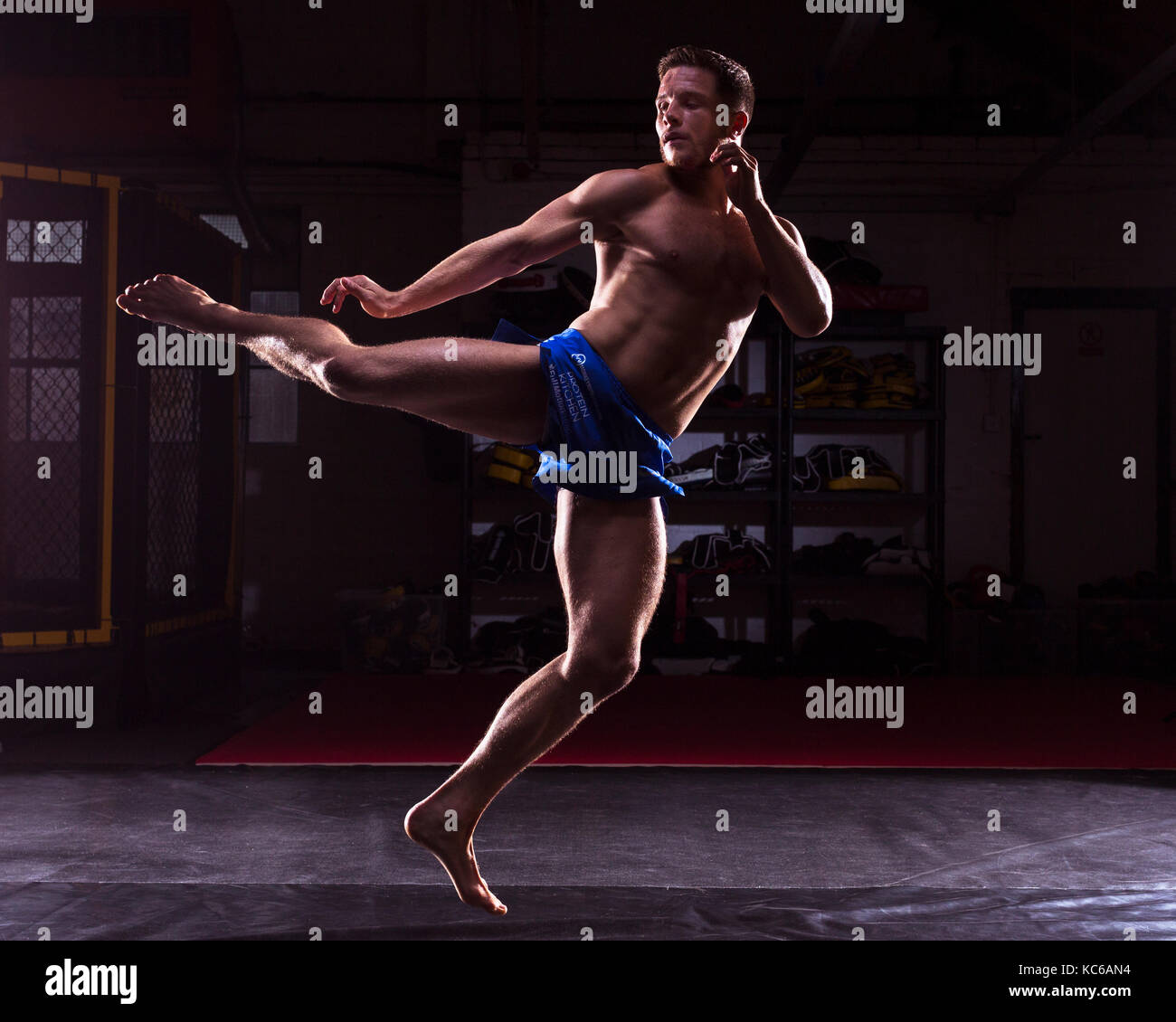 A male MMA fighter training kicks and punches in a dark gym Stock Photo