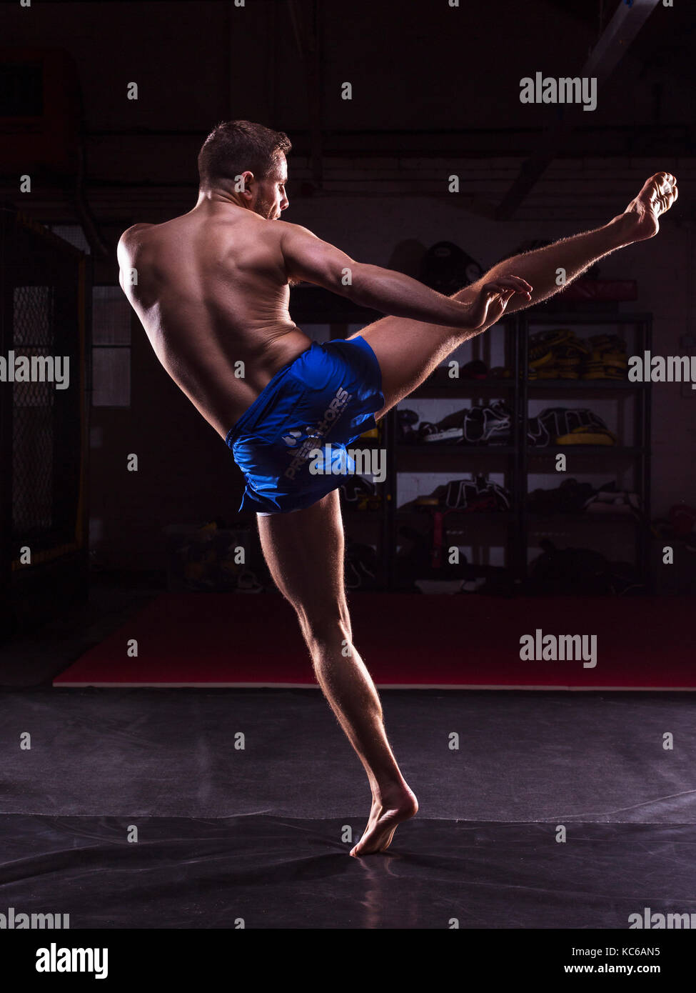 A male MMA fighter training kicks and punches in a dark gym Stock Photo