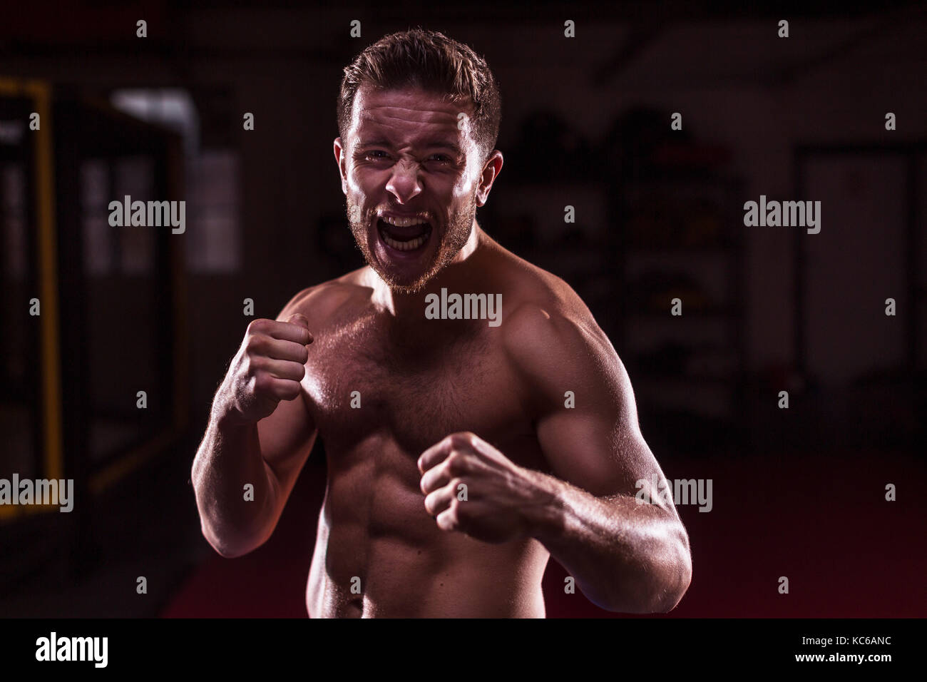 A male MMA fighter training kicks and punches in a dark gym Stock Photo