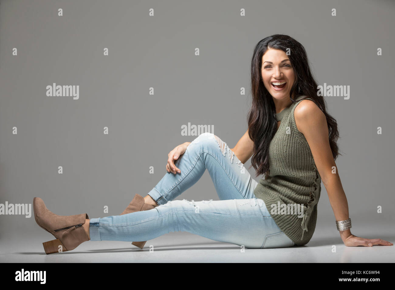 Studio shot of woman sitting on floor and laughing Stock Photo - Alamy