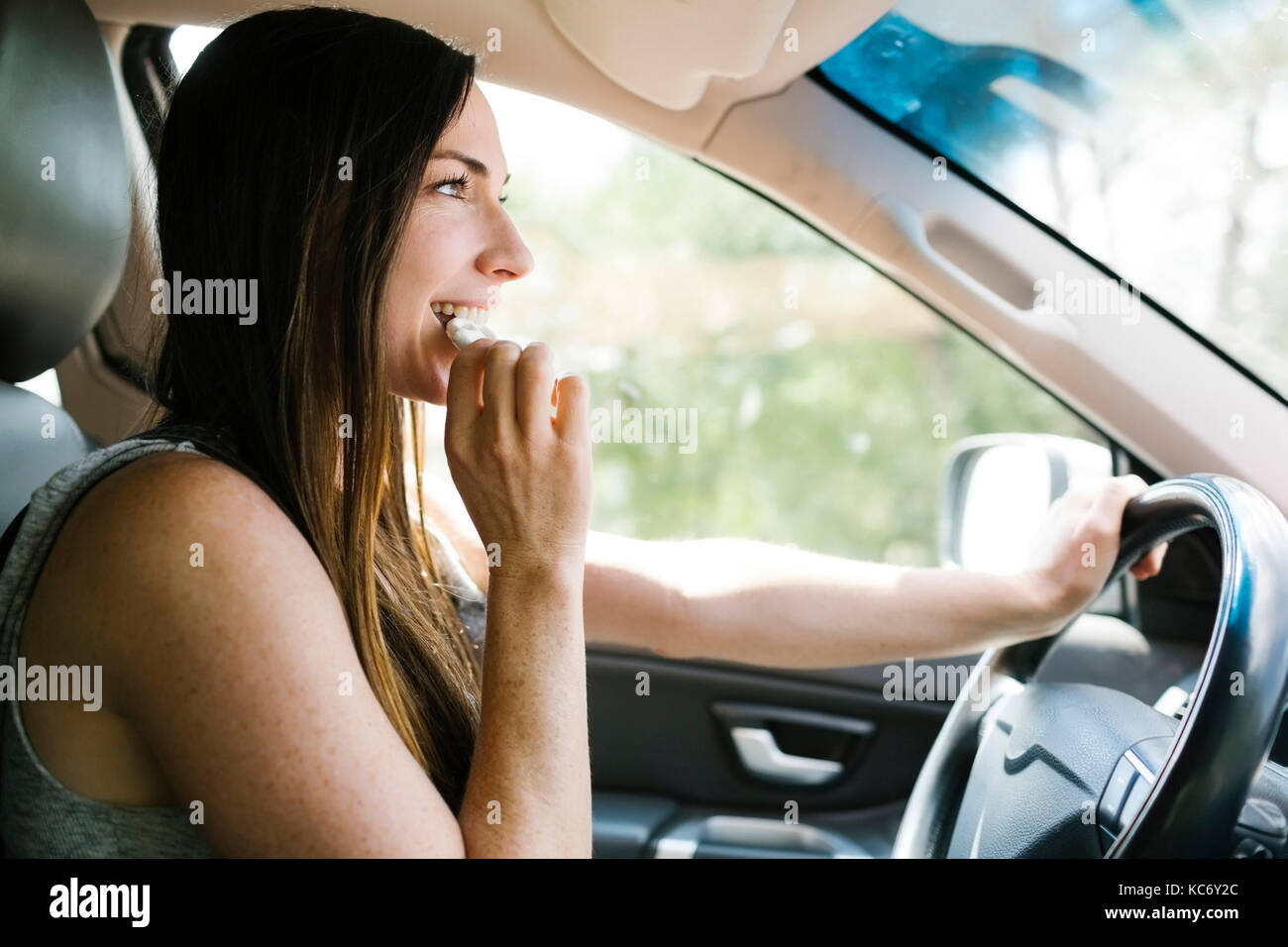 Smiling woman driving car and eating pretzel Stock Photo
