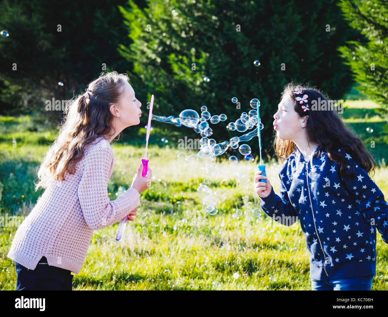 Girls (10-11, 12-13) blowing bubbles in field Stock Photo