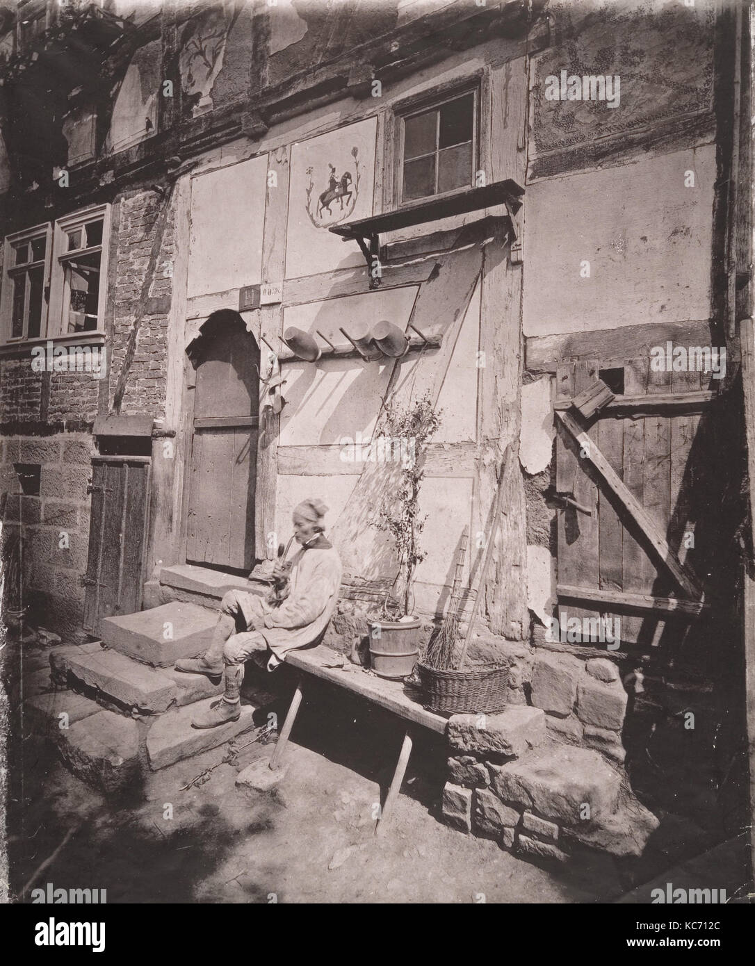 Man Smoking Pipe Outside His Home on Village Street, Unknown, 1880s Stock Photo