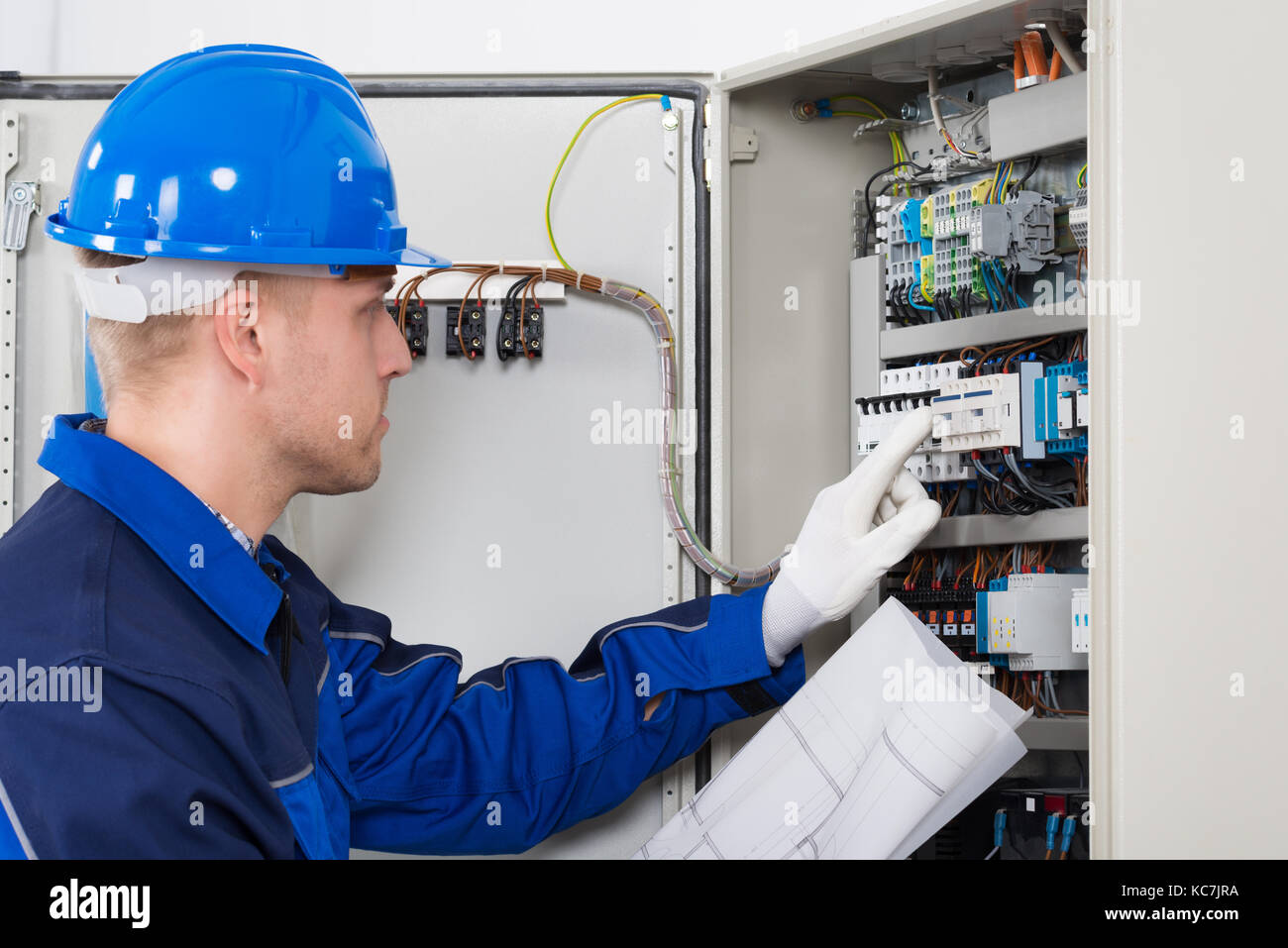 Male Electrician Testing Fusebox With Blueprint In Hand Stock Photo