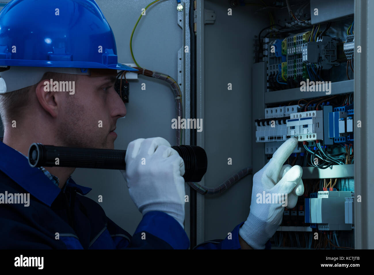 Male Technician Looking At Fusebox With Flashlight Stock Photo