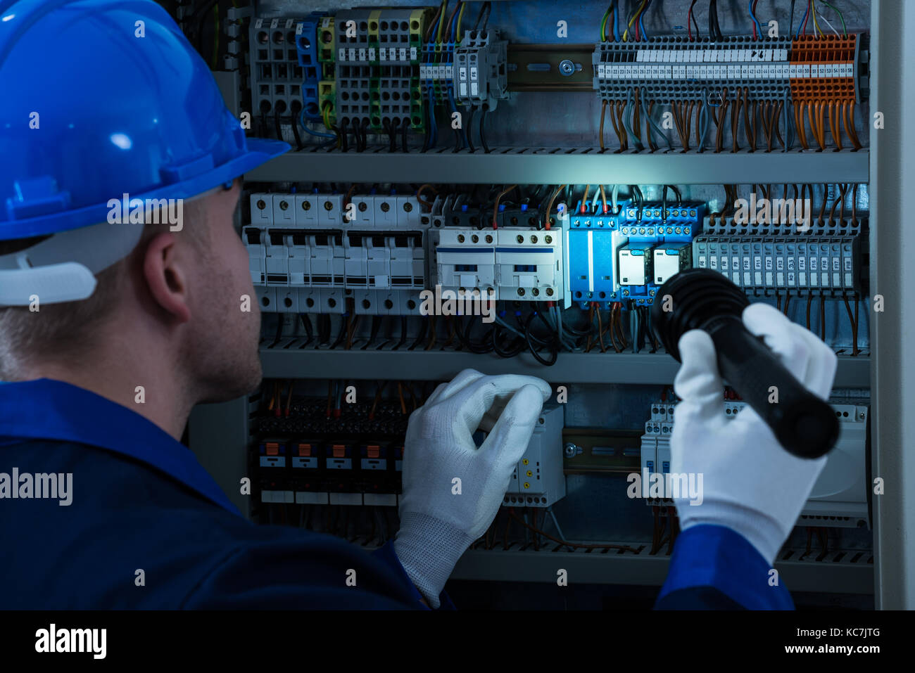 Male Technician Looking At Fusebox With Flashlight Stock Photo