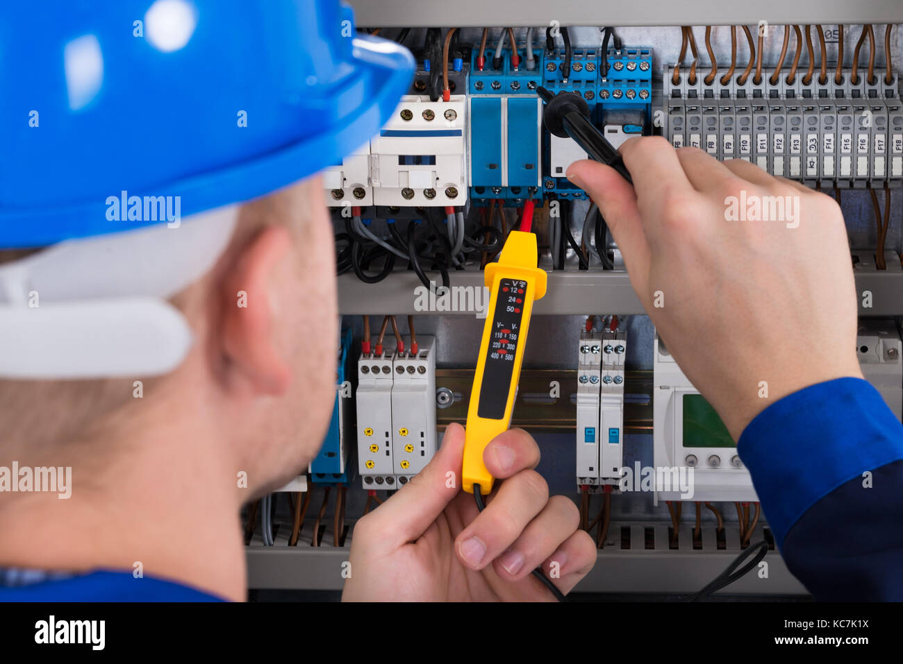 Male Electrician Examining Fusebox With Voltage Tester Stock Photo