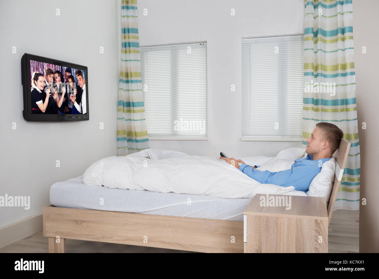 Young Man Leaning On Bed Watching Television Stock Photo