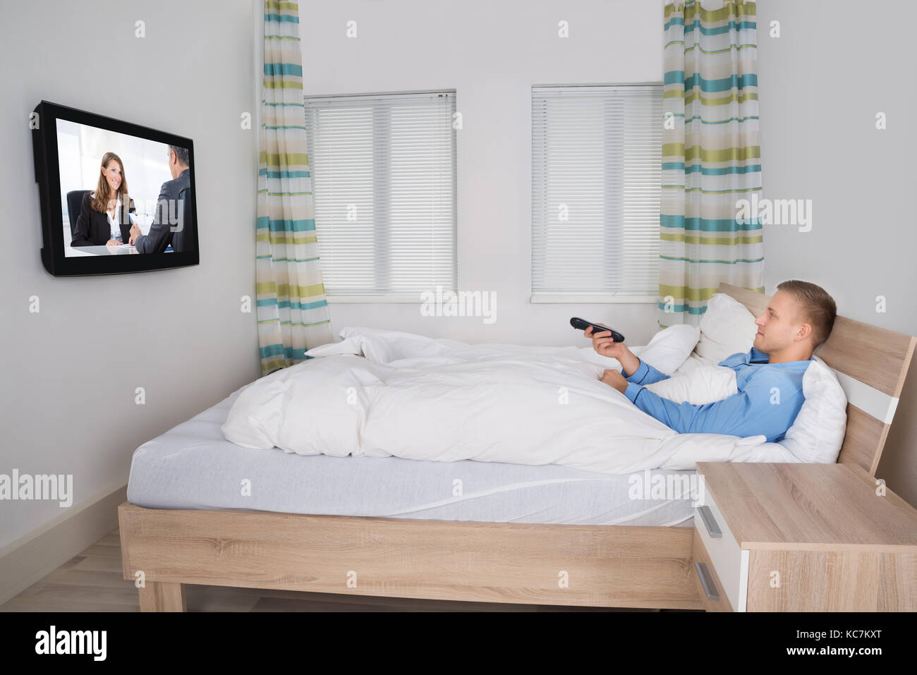 Young Man Holding Remote While Watching Television In His Bedroom Stock Photo