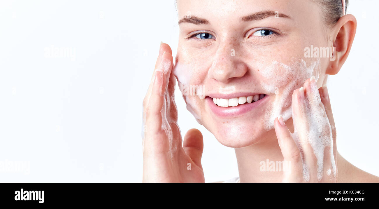 Teenager skincare. Smiling beautiful teen girl with freckles and blue eyes using foaming cleanser. Face washing concept isolated on white background. Stock Photo