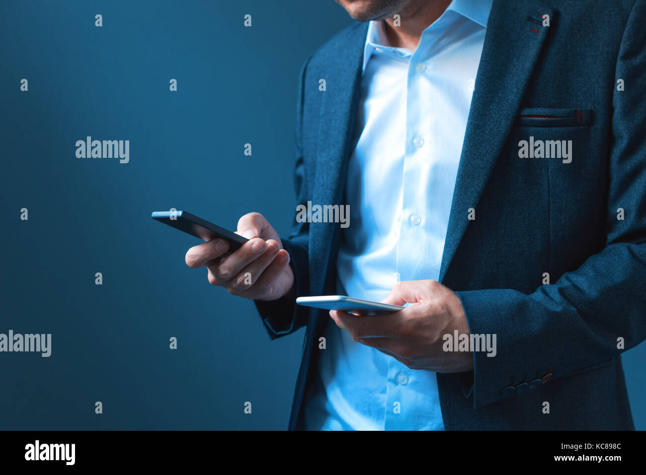 Sync and backup data on two mobile phones, man in business suit synchronizes files, messages and contact information on private and company smartphone Stock Photo