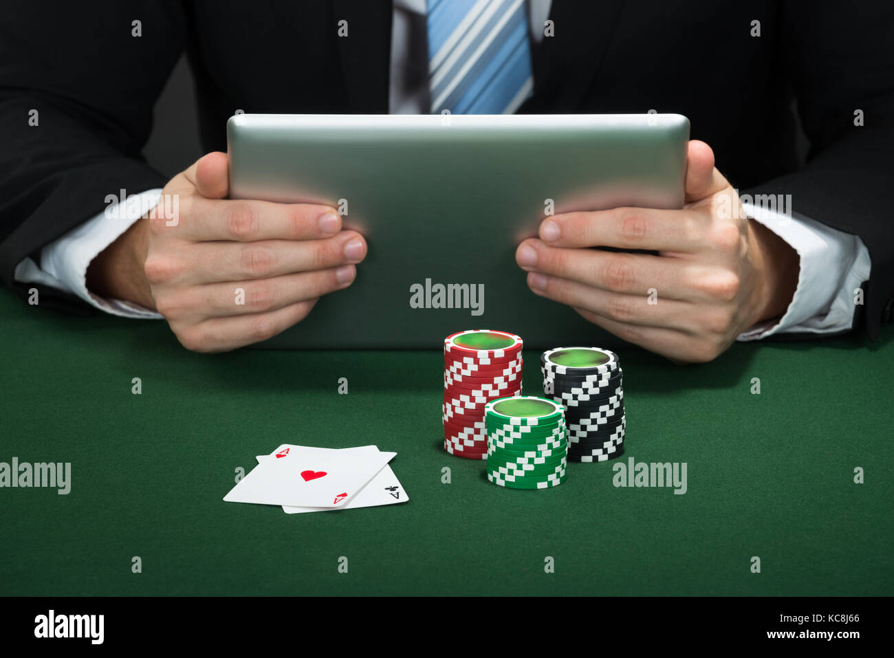 Poker Hand Holding Digital Tablet With Chips And Cards On Table Stock