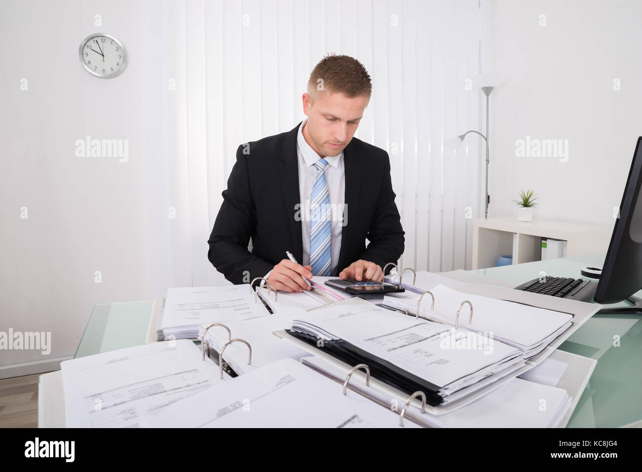 Young Businessman Calculating Tax At Office Desk Stock Photo