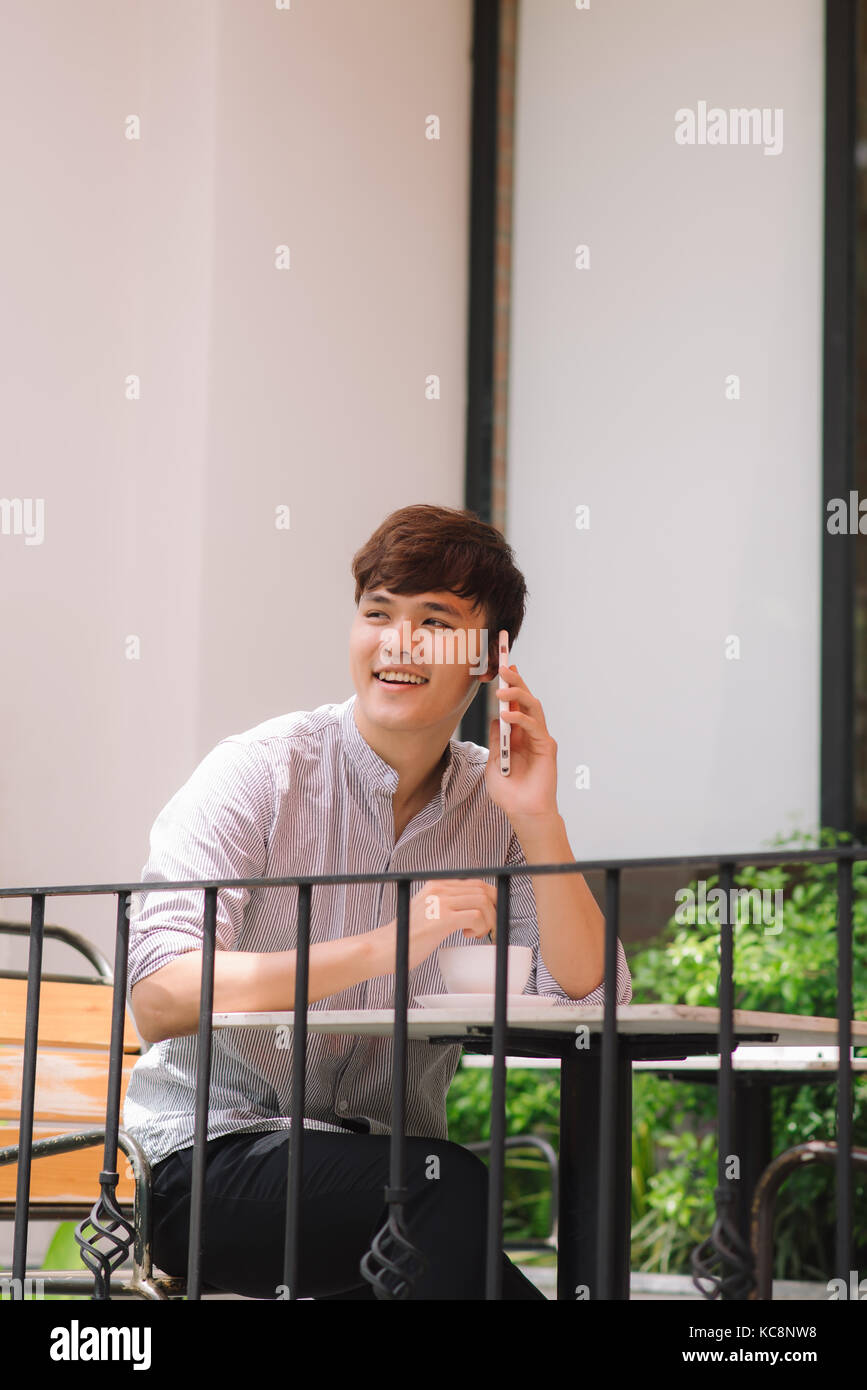 Cheerful young man in casual wear talking on the mobile phone while sitting in cafe. Stock Photo