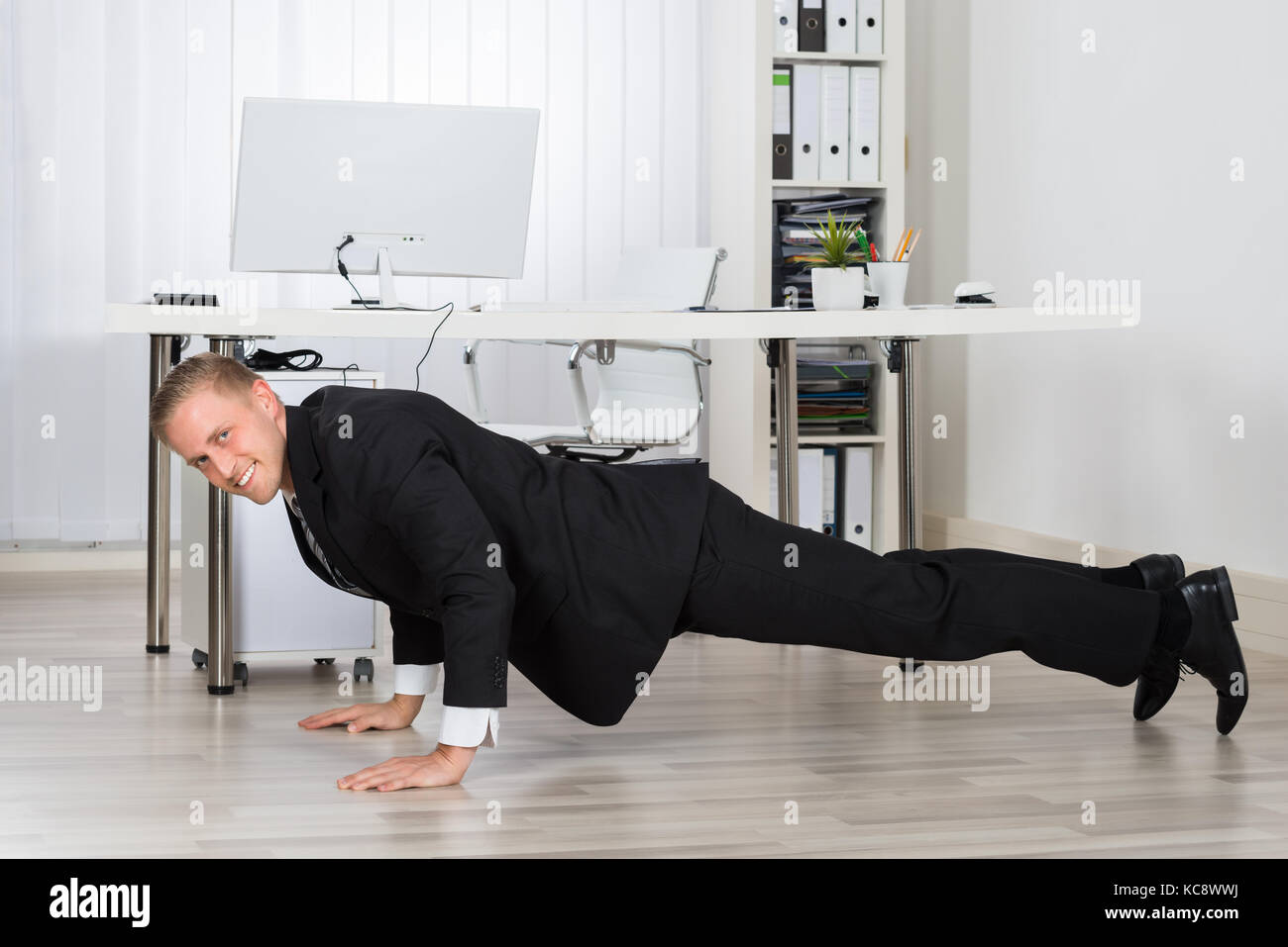 Young Businessman Doing Pushup At Work In Office Stock Photo